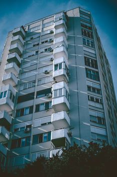 Contemporary urban skyscraper with distinct balconies and moody shadows under a clear sky.