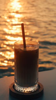 Glass of iced coffee on a table by the sea with a beautiful sunset reflection.