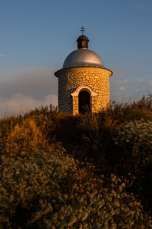 Free A picturesque stone chapel sits atop a hill, bathed in warm sunset light, surrounded by wildflowers. Stock Photo