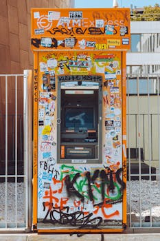 Vibrant ATM covered in stickers and graffiti, captured on a bright day.