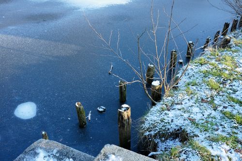 Free A tranquil view of a partially frozen lake with snow on the grassy shore. Stock Photo