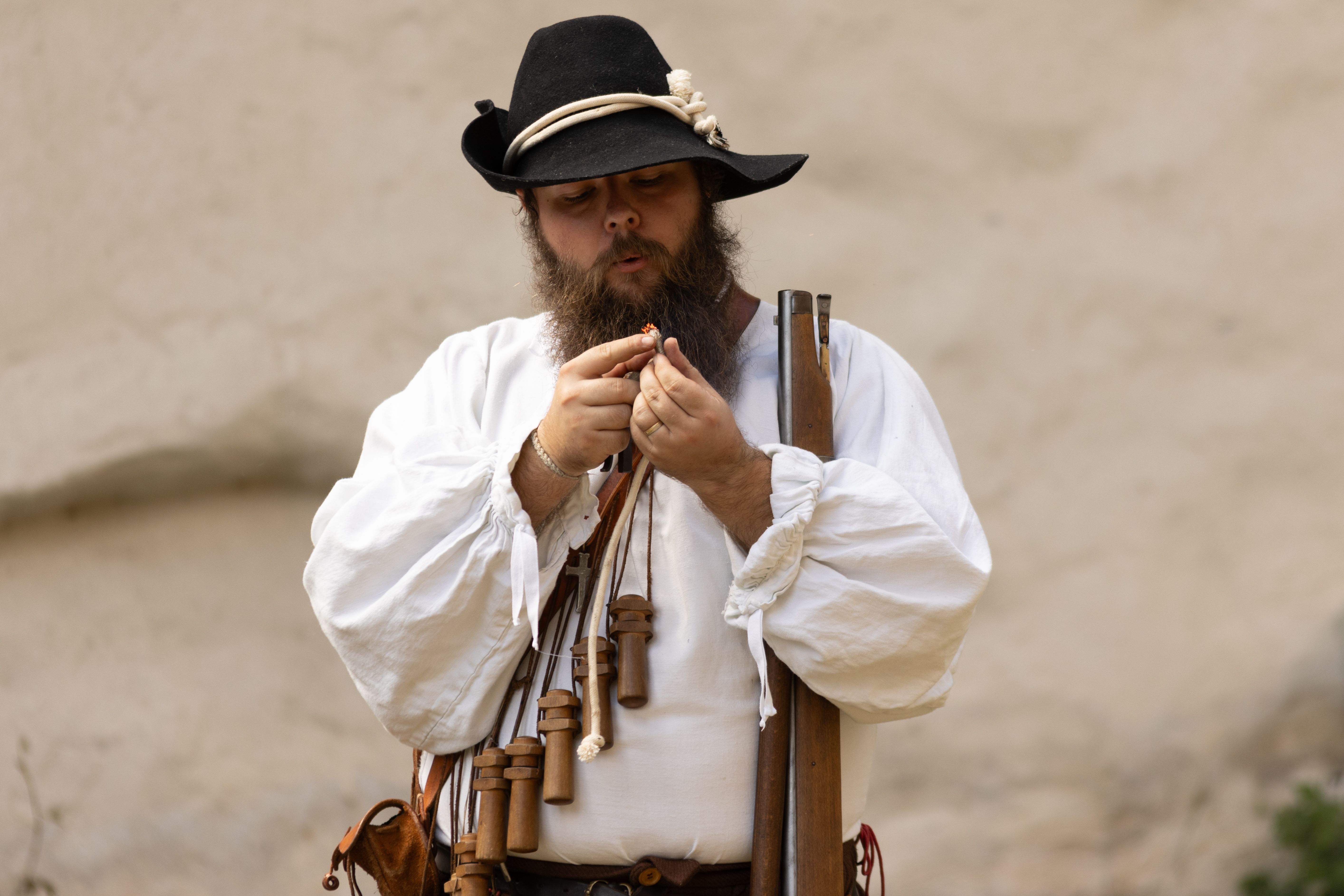 Man in historical clothing loading a musket outdoors, reenactment setting.