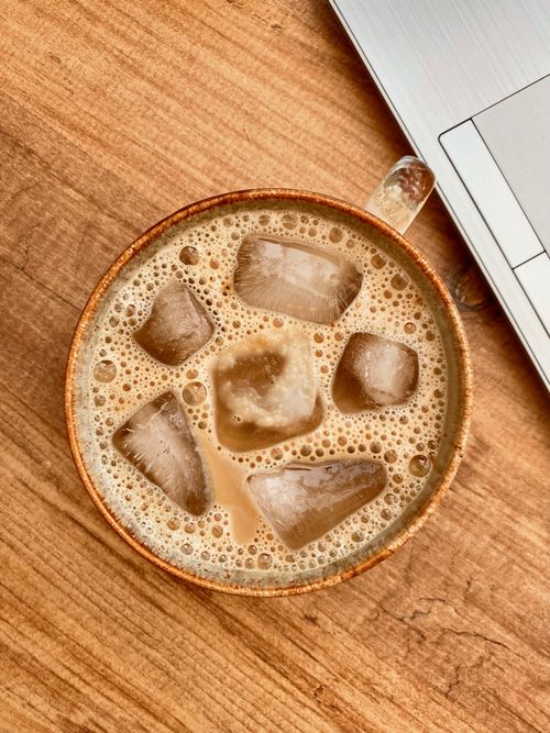 Free Iced coffee in earthenware mug on rustic wooden table next to laptop. Stock Photo