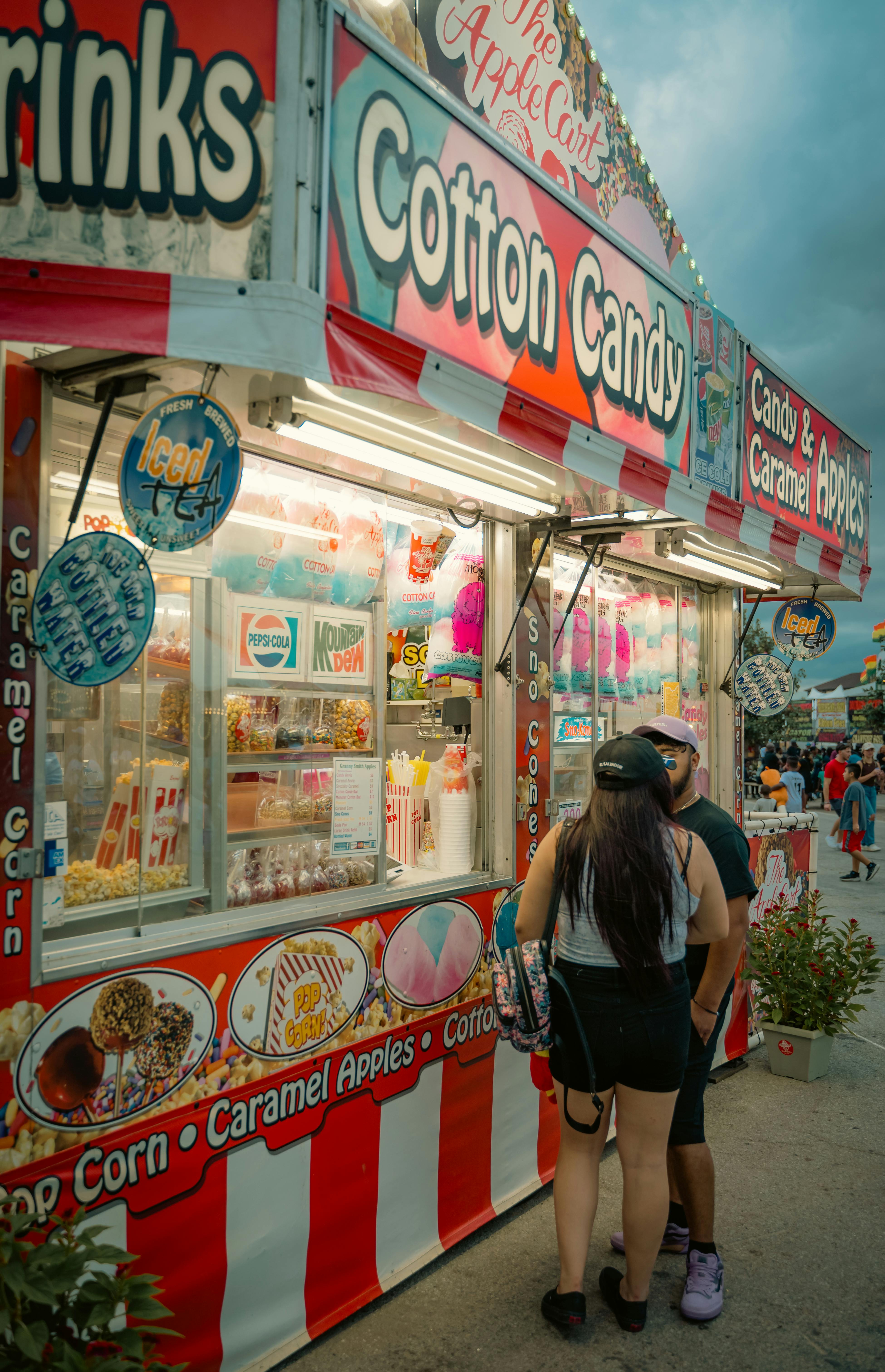 a couple standing in front of a carnival food stand