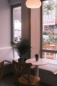 Cozy cafe interior with a modern design, featuring a round table and chairs near large windows.