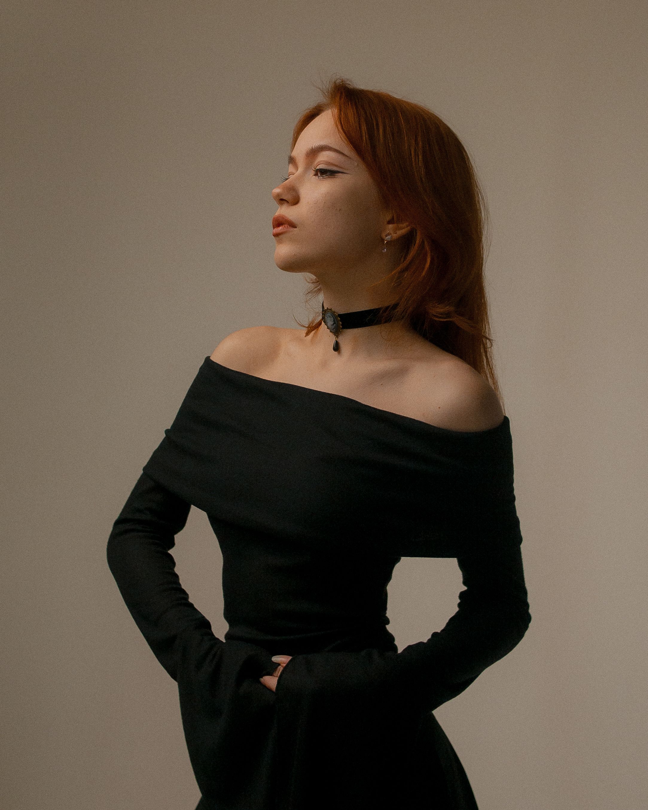 Stylish portrait of a woman with red hair wearing an off-shoulder black dress and a choker, exuding elegance and confidence.