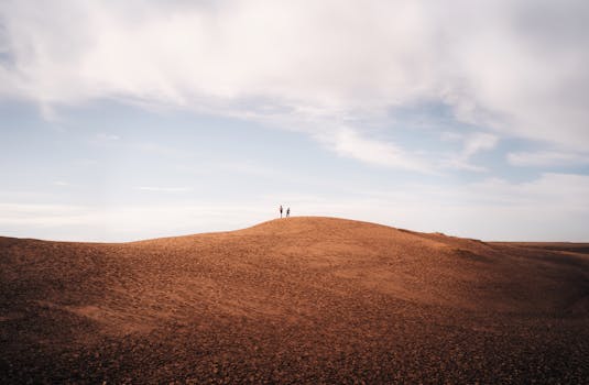 Two people standing on a desert dune under a wide sky in Mendoza, Argentina.