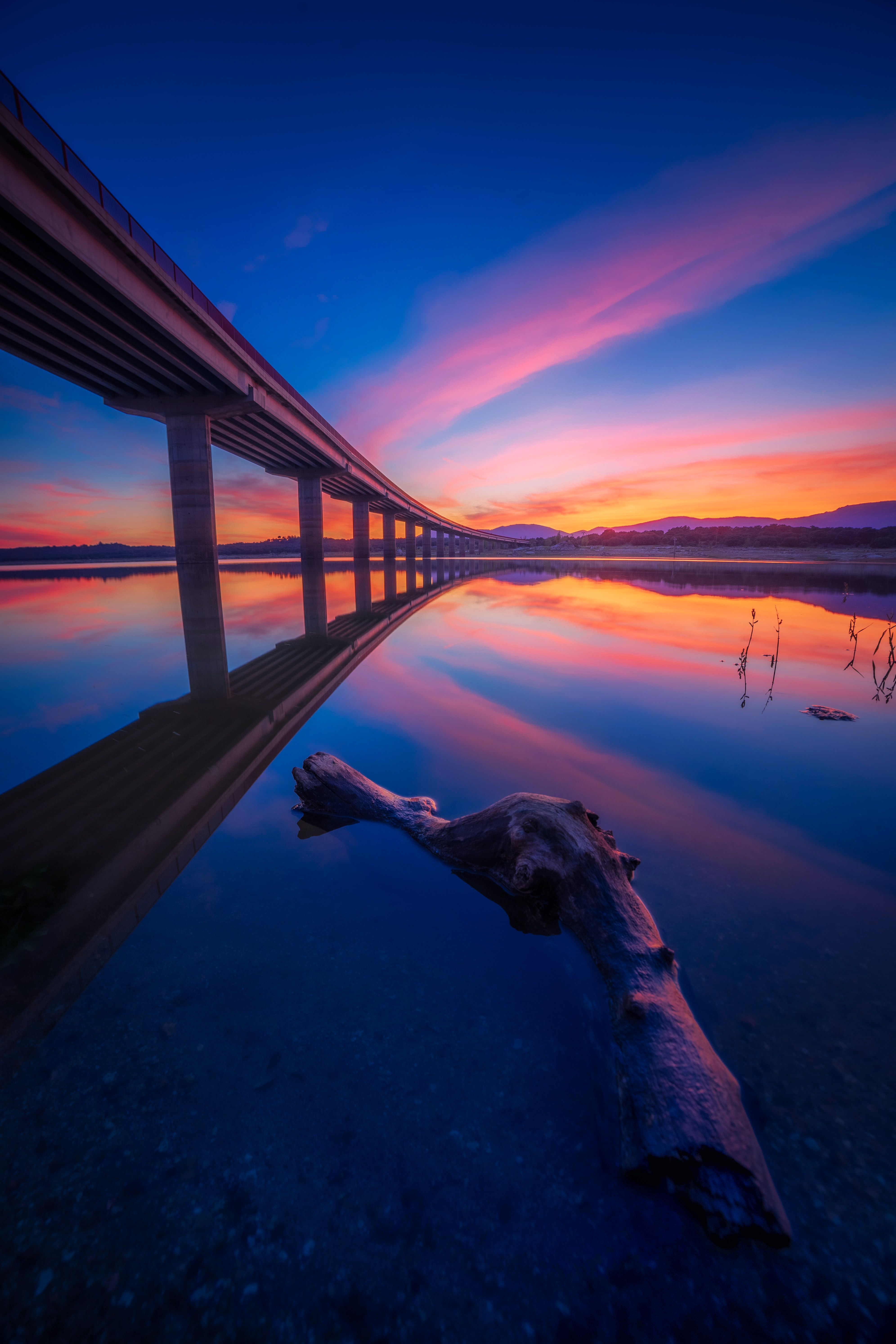 A sunset over a bridge with a reflection in the water · Free Stock Photo