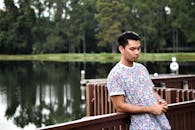 一个年轻人穿着时髦衬衫，若有所思地靠在湖边的木栏杆上
