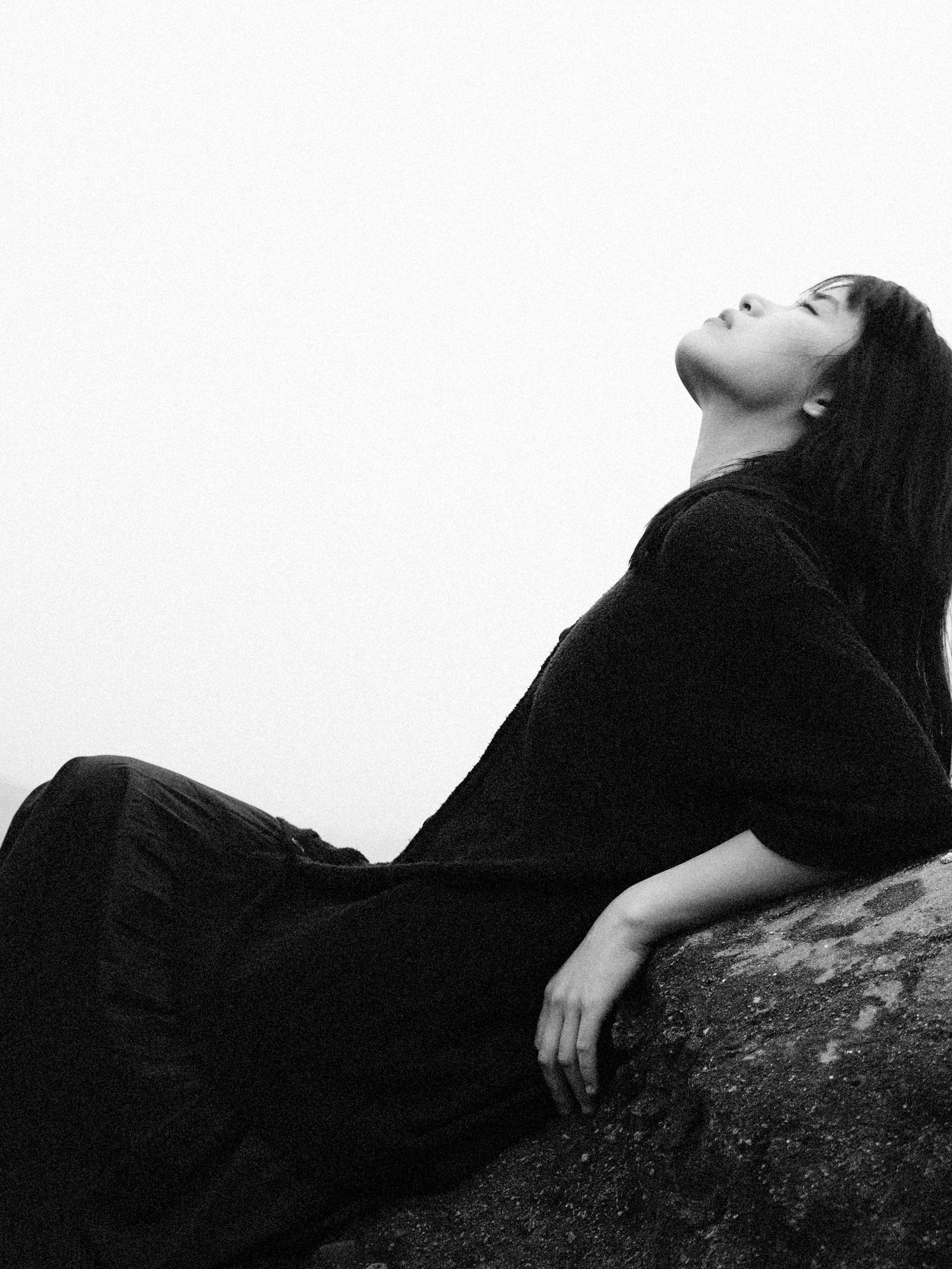 A serene black and white portrait of a woman sitting on a rock, looking contemplative.
