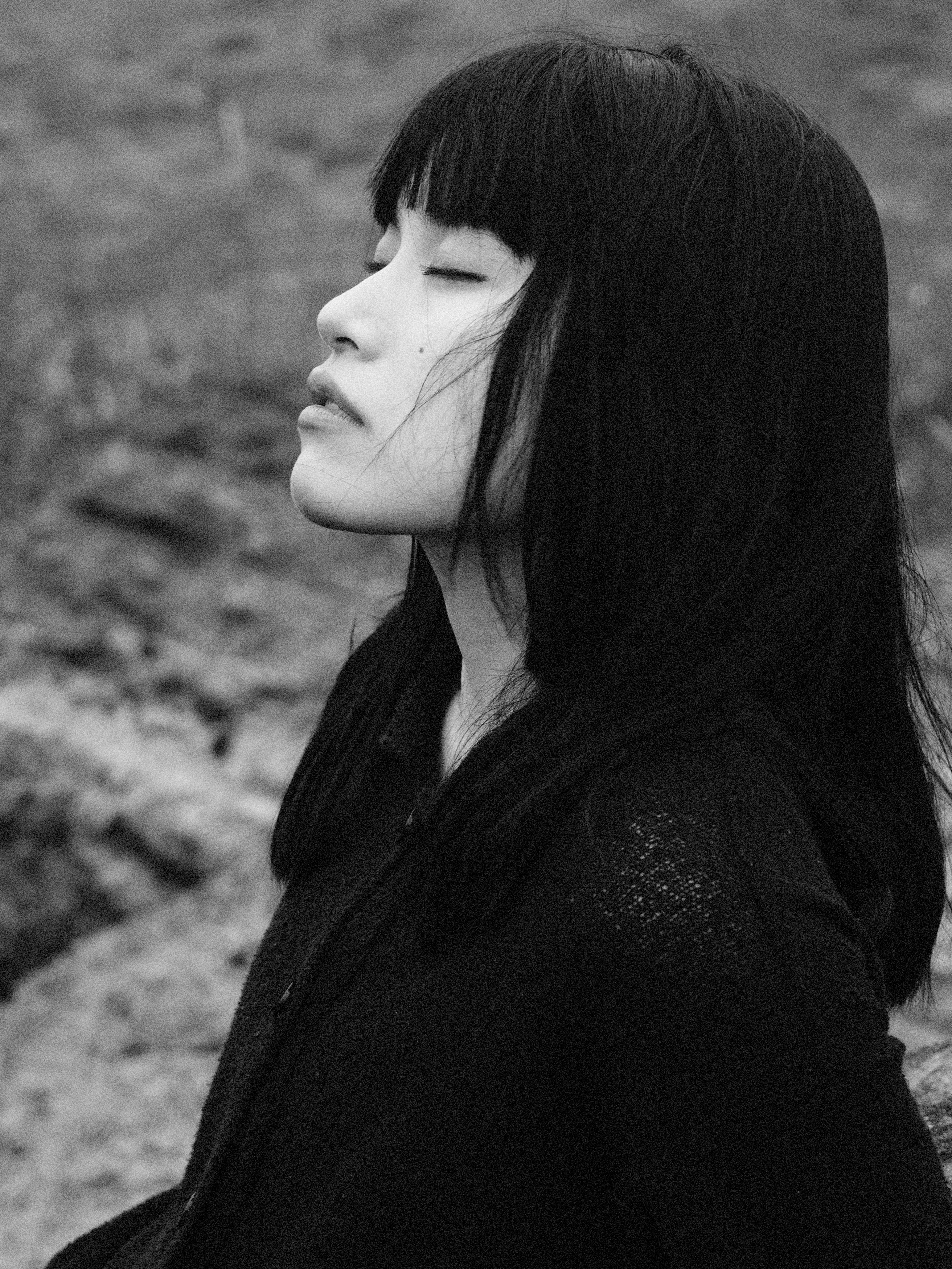 Artistic black and white portrait of a woman with closed eyes in a natural setting.