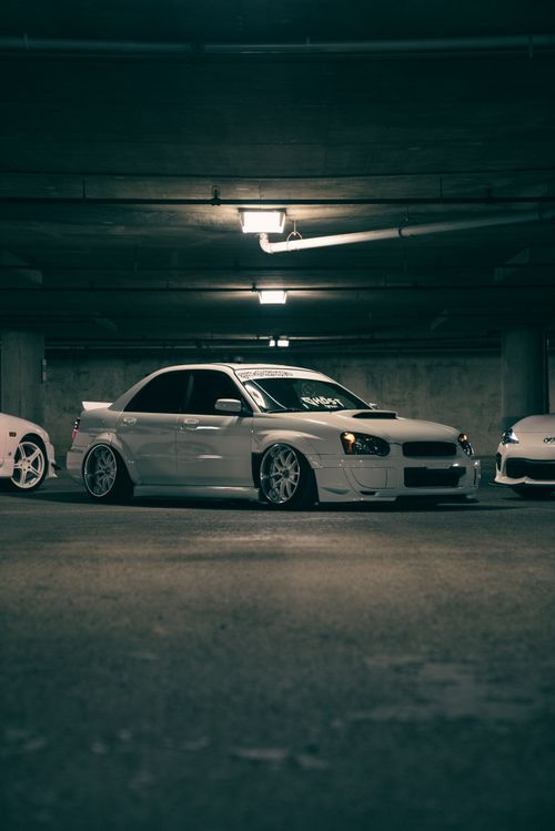 Free Low angle view of a sleek white car in an underground parking garage with moody lighting, emphasizing automotive design. Stock Photo