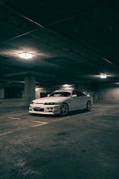 A stylish white sports car parked in a dimly lit underground garage, showcasing a moody atmosphere.