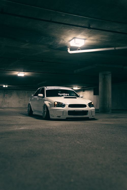 Free White car parked in an underground garage with moody lighting, showcasing modern automotive design. Stock Photo