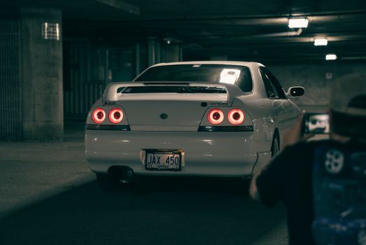 A classic white sports car with red taillights parked in a dimly lit underground garage.