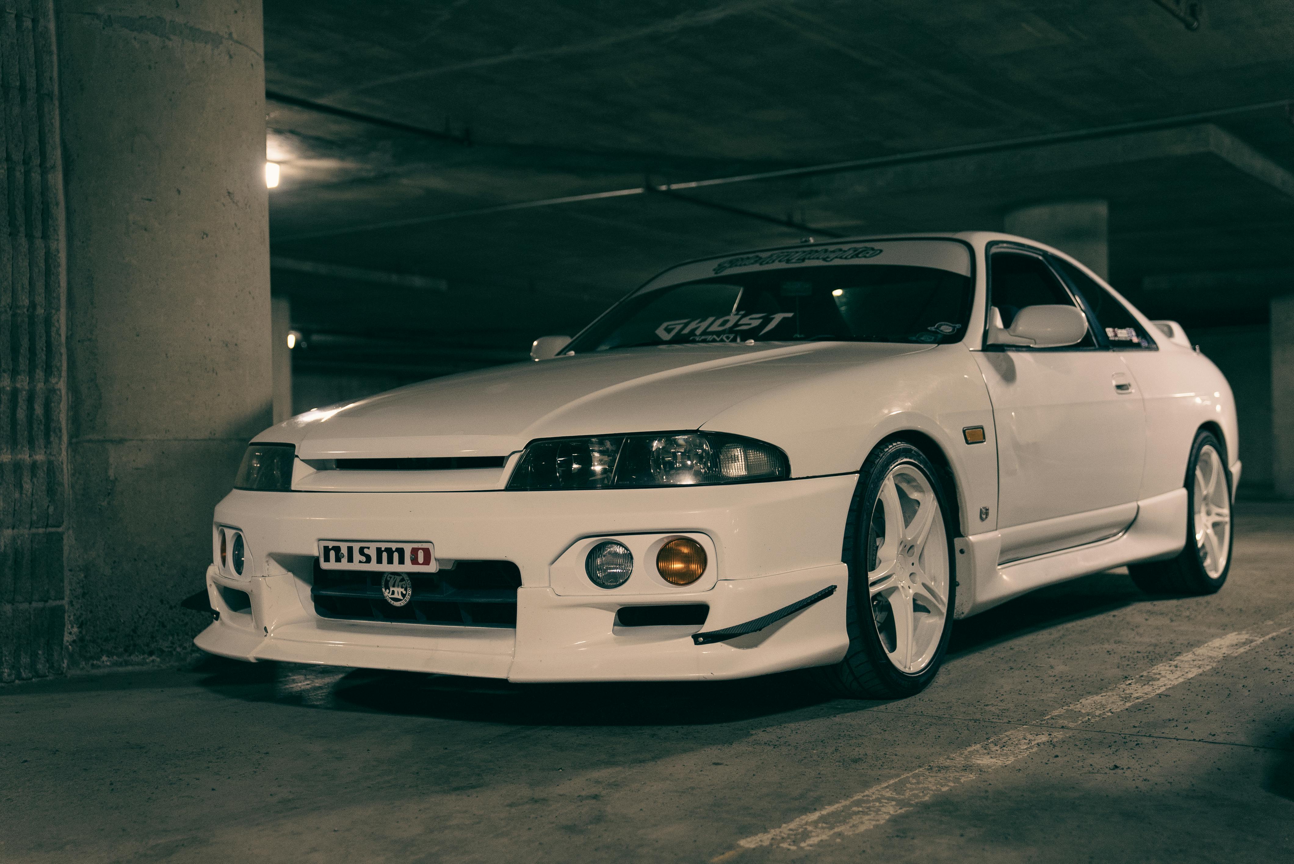 White Nissan sports car parked in an underground garage, showcasing sleek design and modifications.