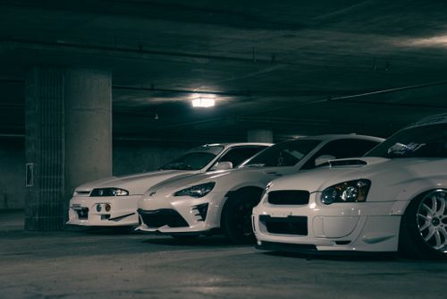 Free Three white sports cars parked in a dimly lit underground garage, showcasing sleek automotive design. Stock Photo