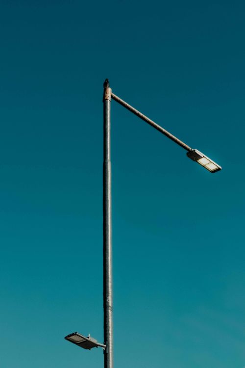 Free A lone streetlight standing against a vibrant blue sky, highlighting urban infrastructure. Stock Photo
