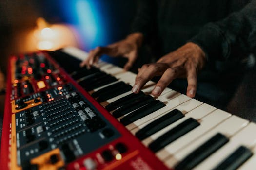 Close-up of hands playing a synthesizer keyboard in a moody, dimly lit environment.