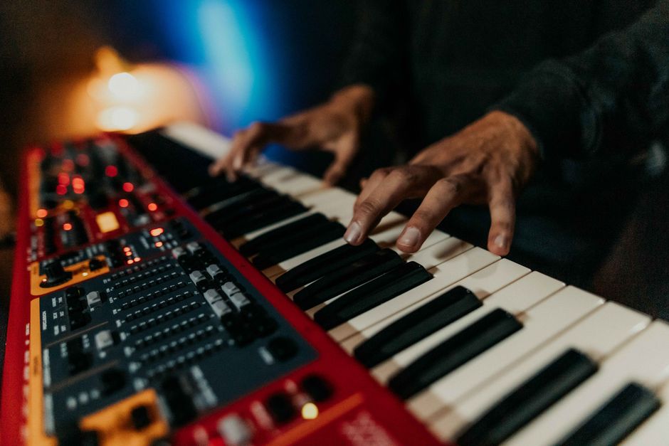 Hands on a synthesizer keyboard in low light. Pexels photo by Gera Cejas.