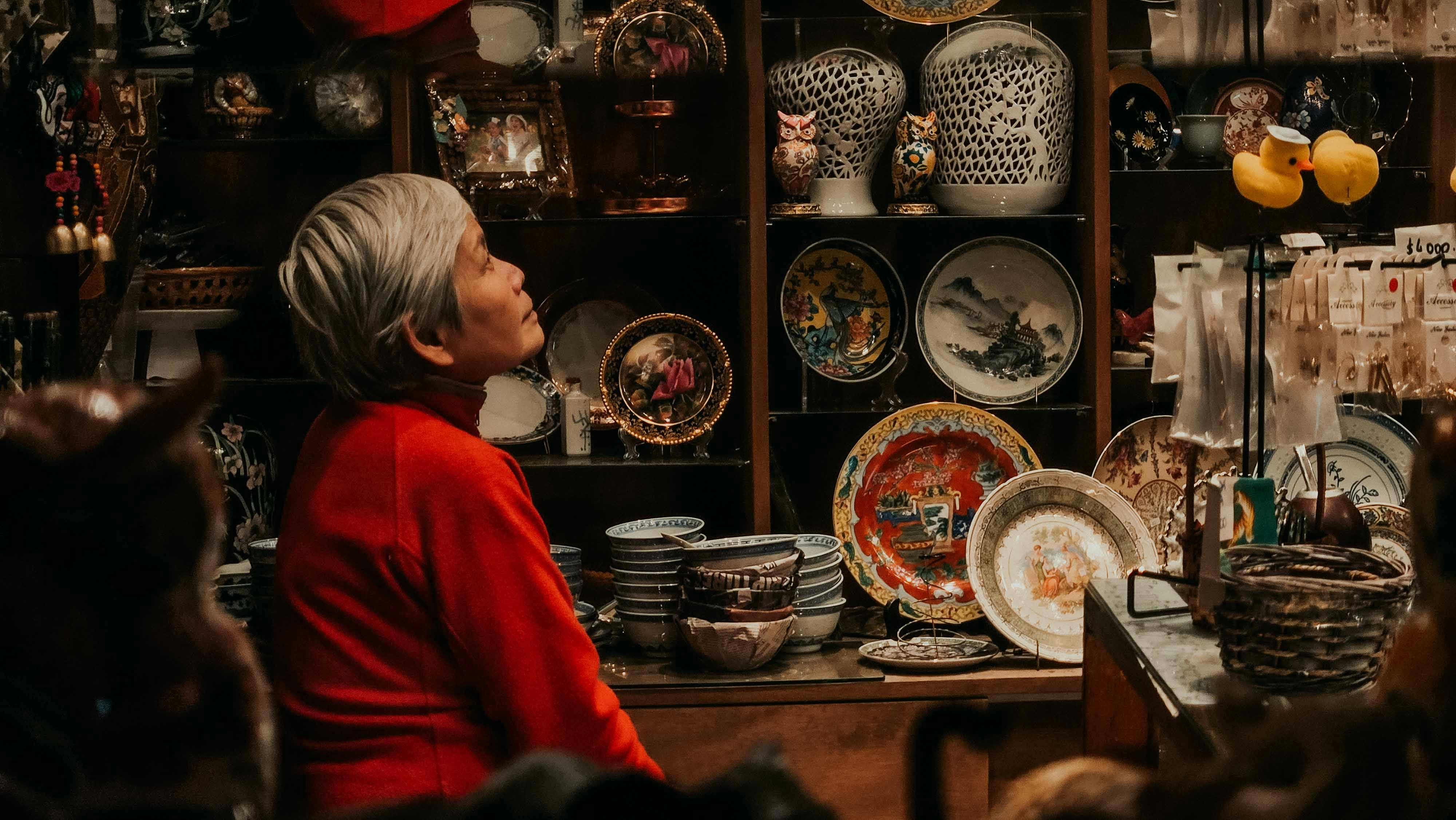Elderly person with gray hair surrounded by traditional pottery in an artisan shop.