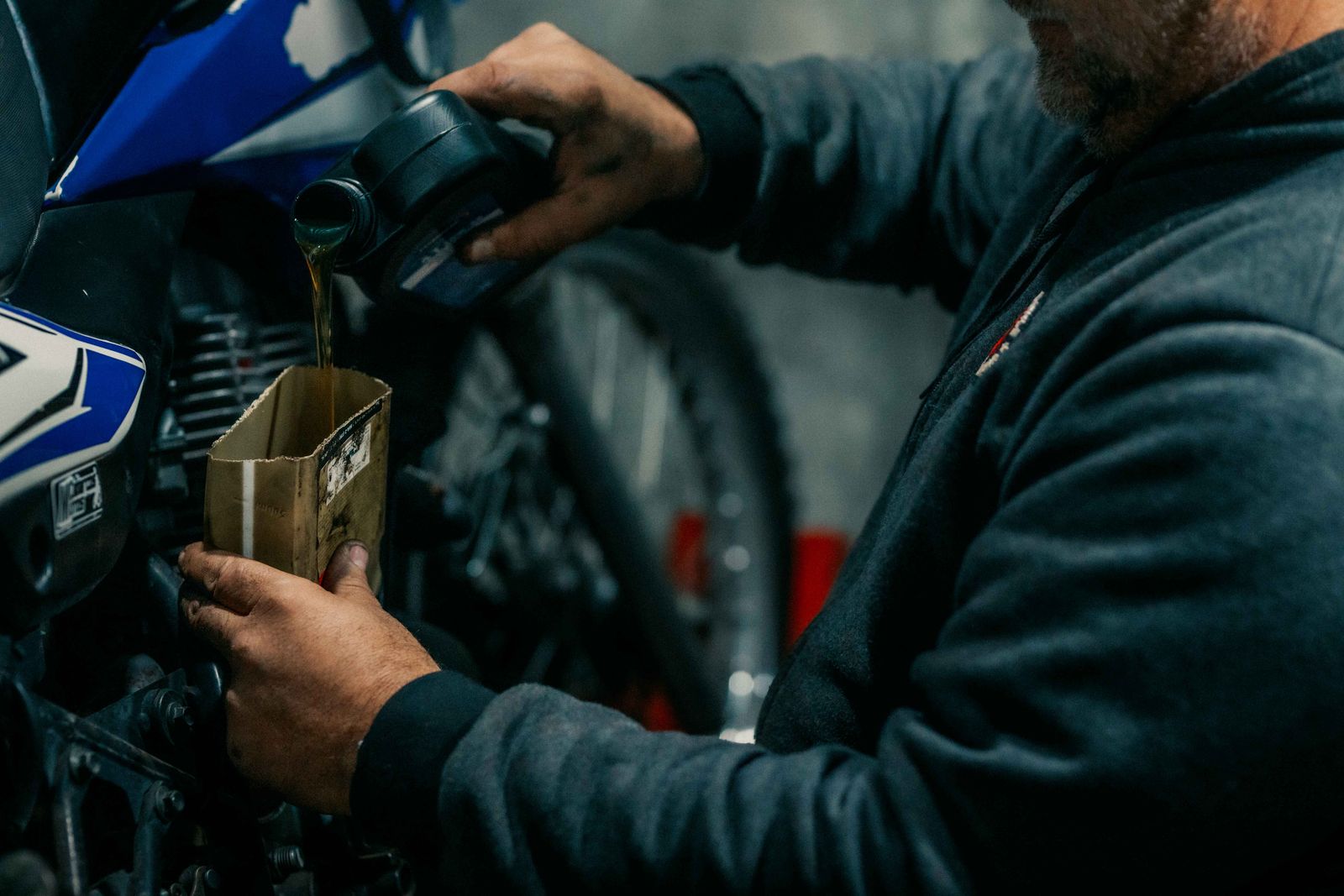 Mécanicien versant de l'huile dans le moteur d'une moto dans un garage faiblement éclairé