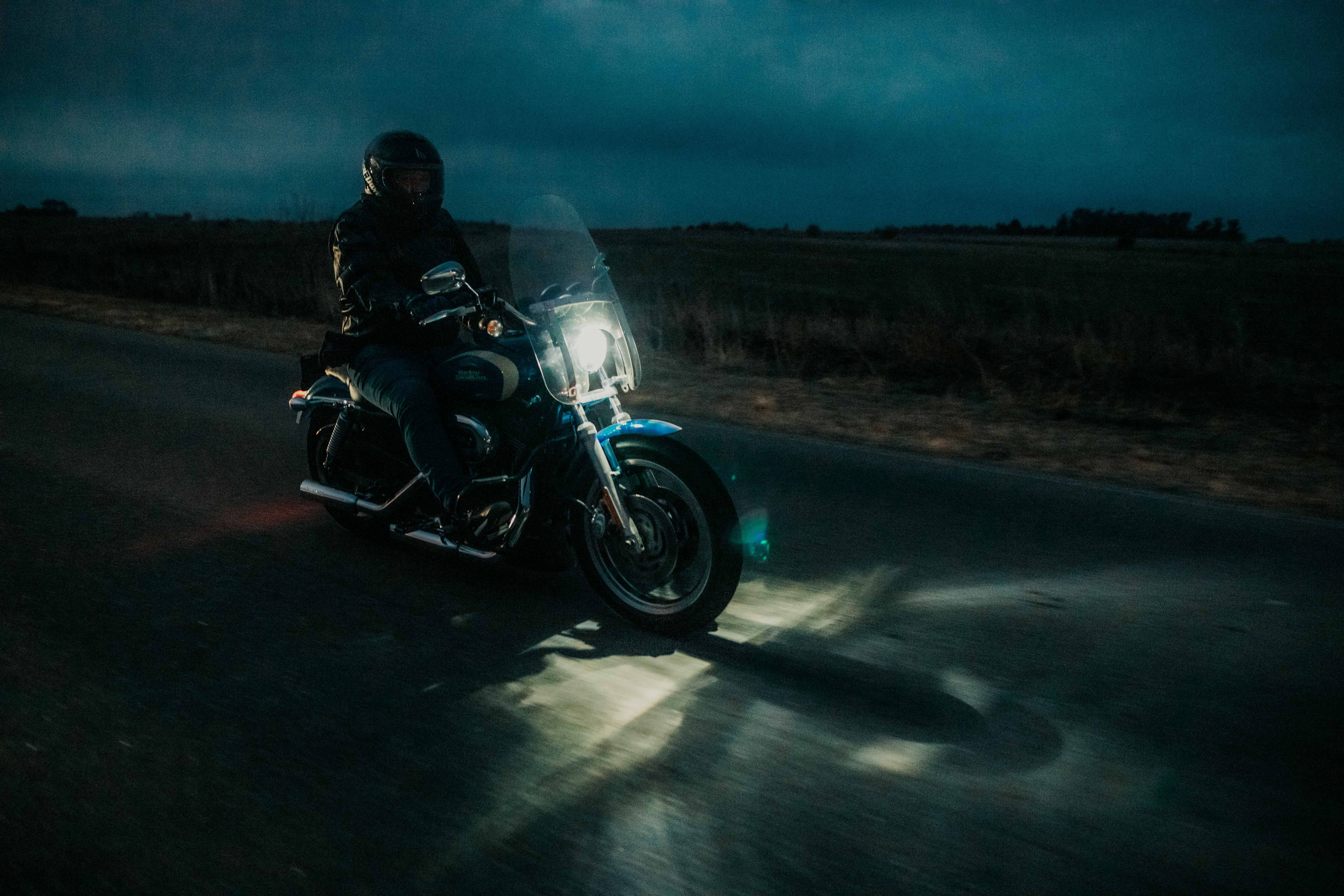 A motorcyclist rides under the night sky, headlight illuminating the open road.