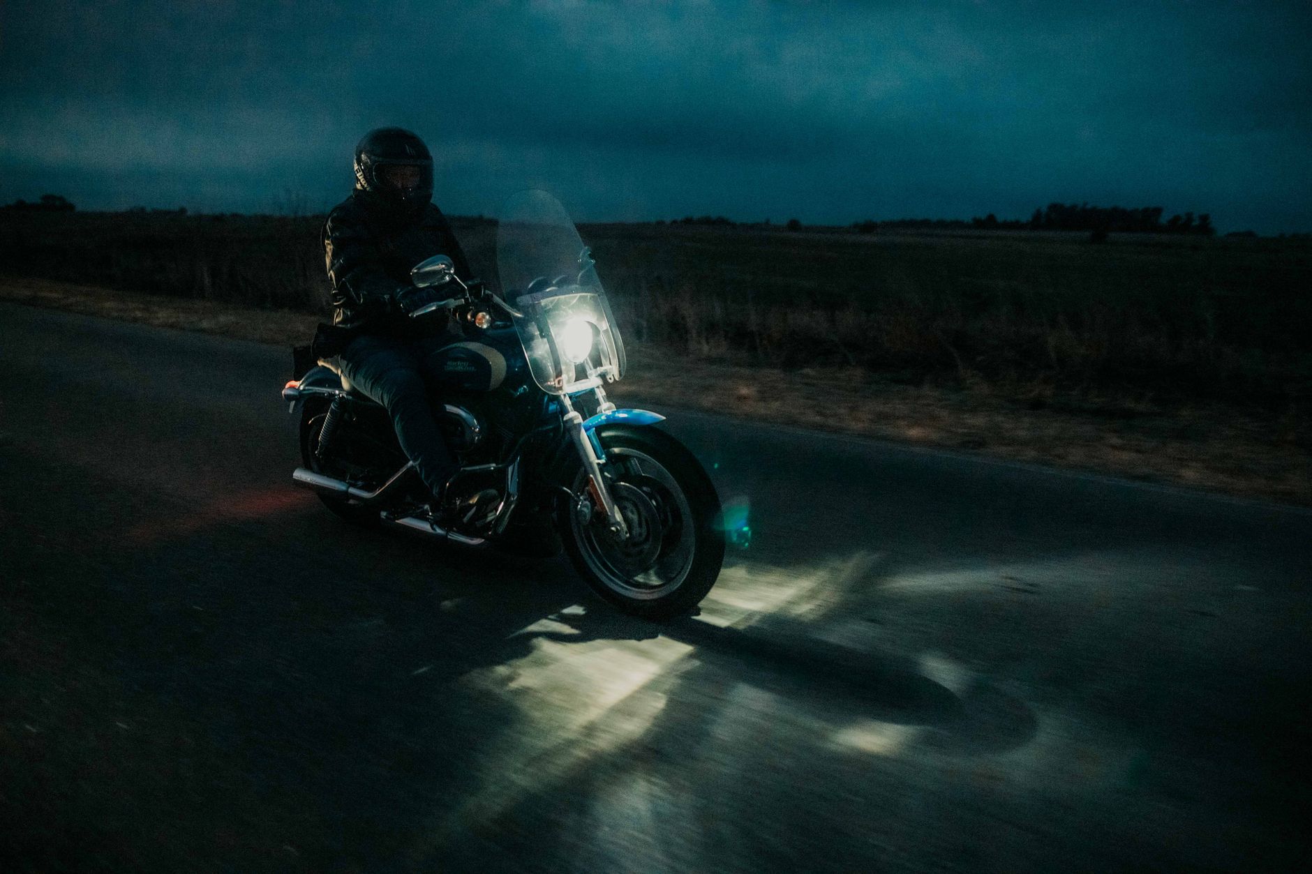 A motorcyclist rides under the night sky, headlight illuminating the open road.