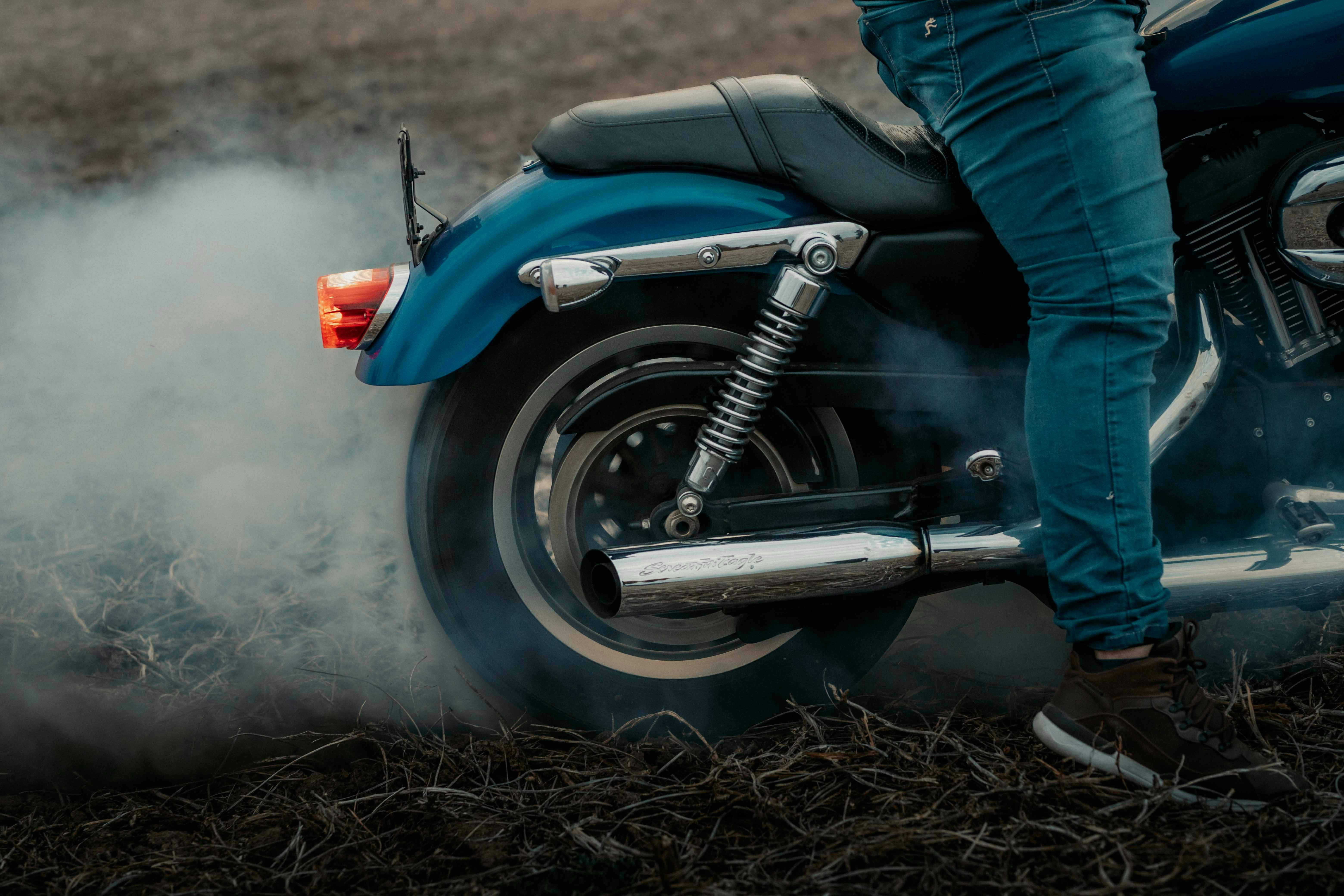 Rear view of a motorcycle and rider performing a burnout on a dirt surface with smoke