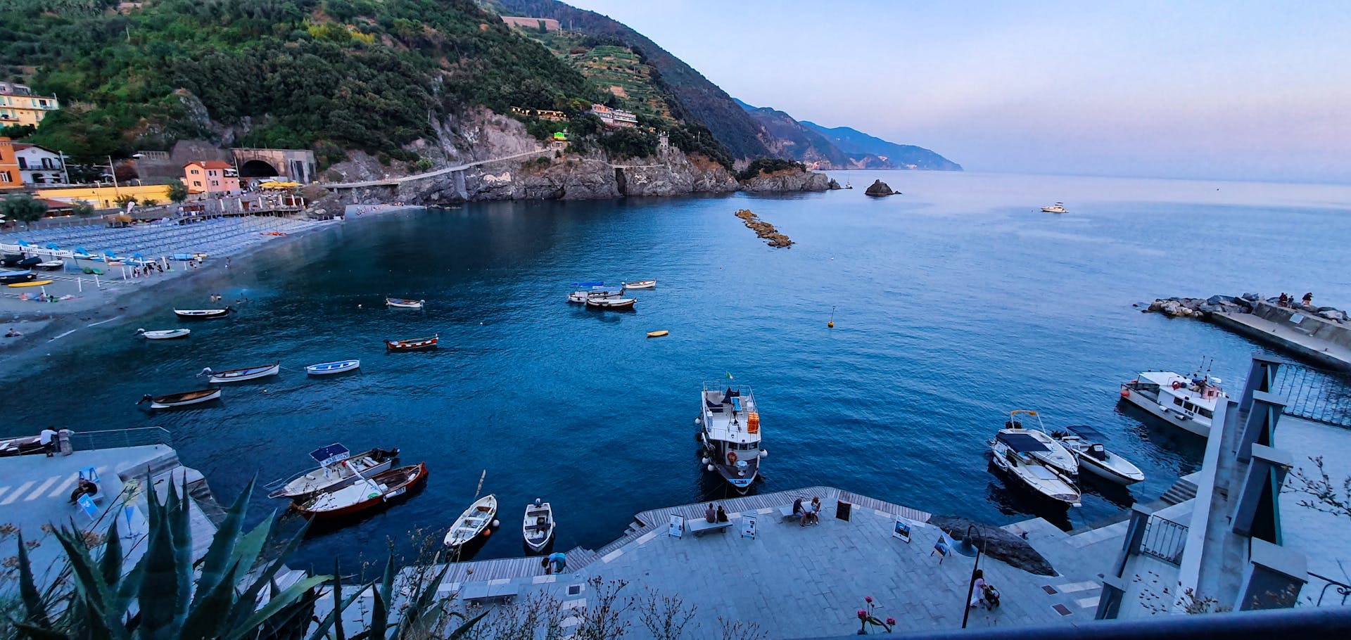 Peaceful harbor with boats surrounded by cliffs and a calm sea at dusk.