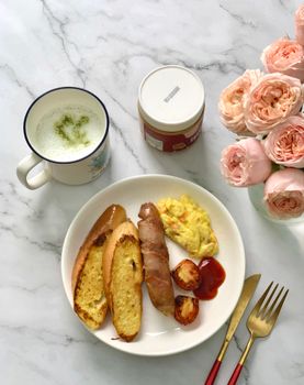 A delightful breakfast with sausages, bread, and matcha latte, accented by a bouquet of roses.
