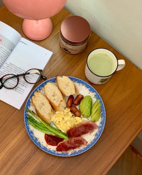 A cozy breakfast plate with bread, meat, and vegetables beside a book. Perfect morning vibe.