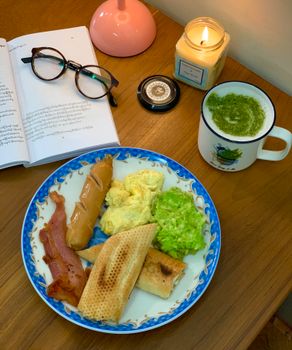 A cozy breakfast scene with scrambled eggs, bacon, and a cup of green coffee.