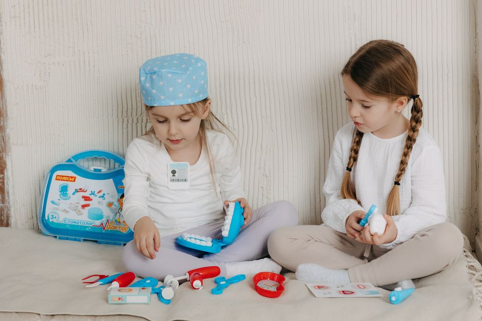 Duas meninas jovens brincando de dentistas com um kit dental de brinquedo dentro de casa.