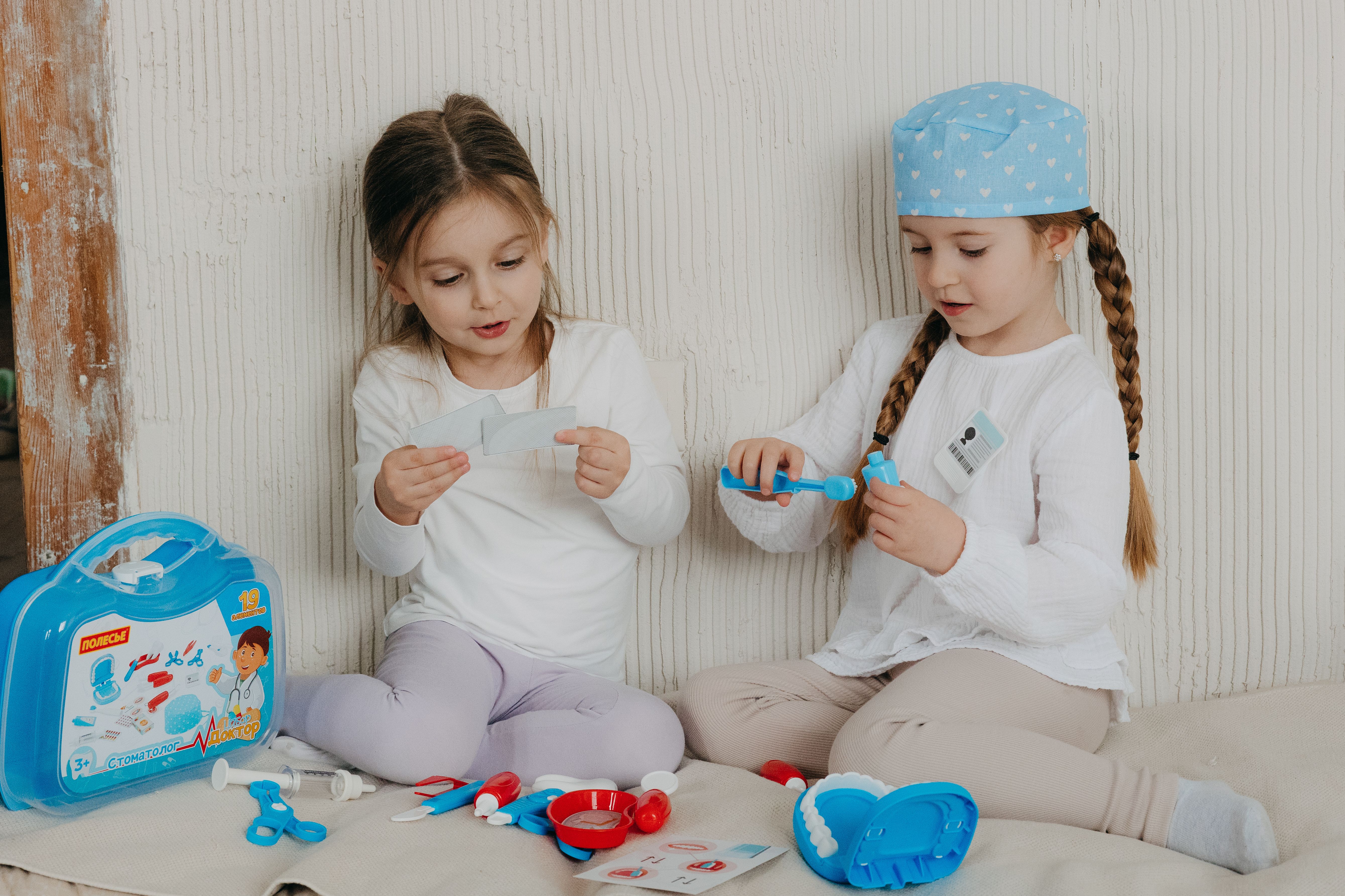 Two young girls playing dentist with toy kit indoors, promoting imaginative play.