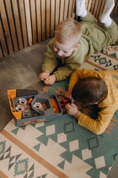 Two boys engaged in play with a toy indoors, lying on a patterned carpet.
