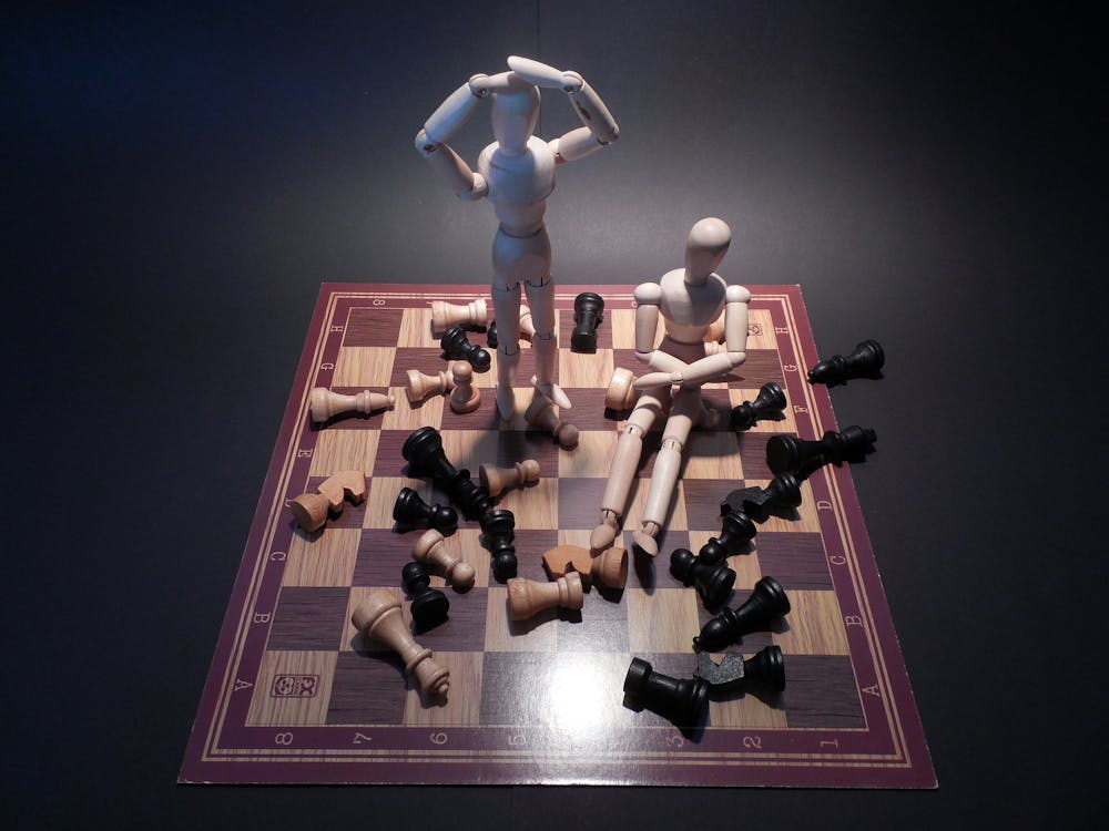 Two White Wooden Mannequins on Wooden Chess Board