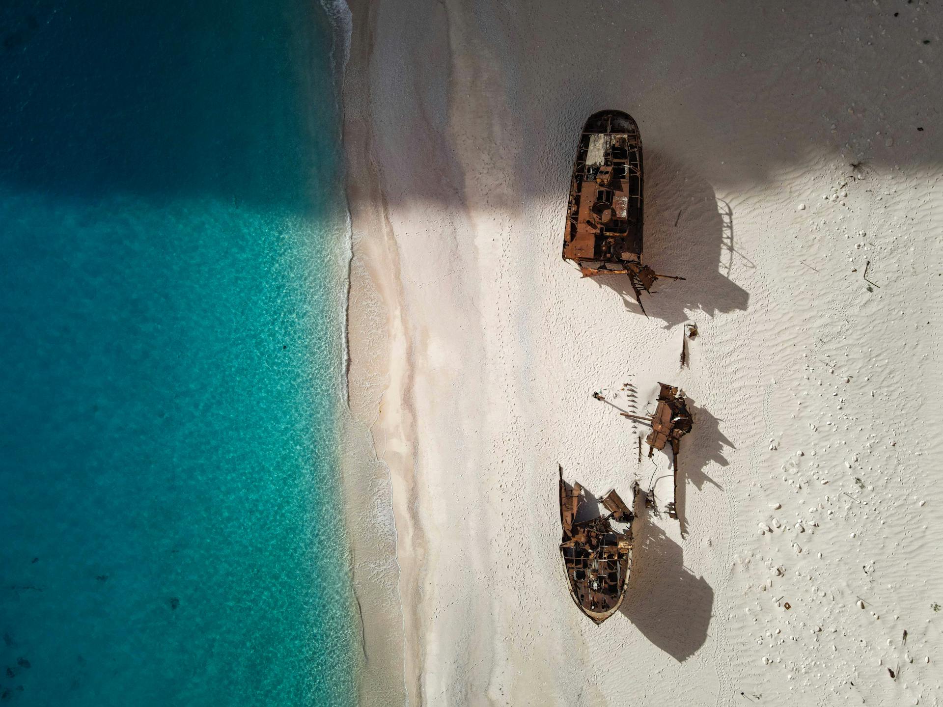 Shipwreck remains on a pristine sandy beach with turquoise waters, viewed from above.