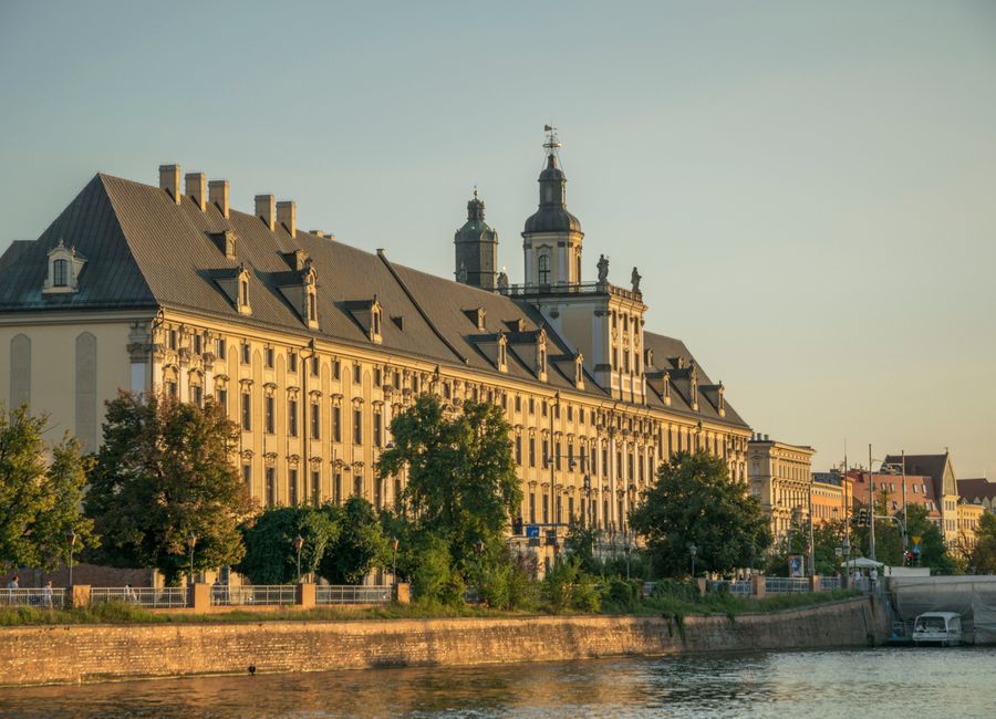 Scenic view of the historic Wrocław University building along the Odra River at sunset.