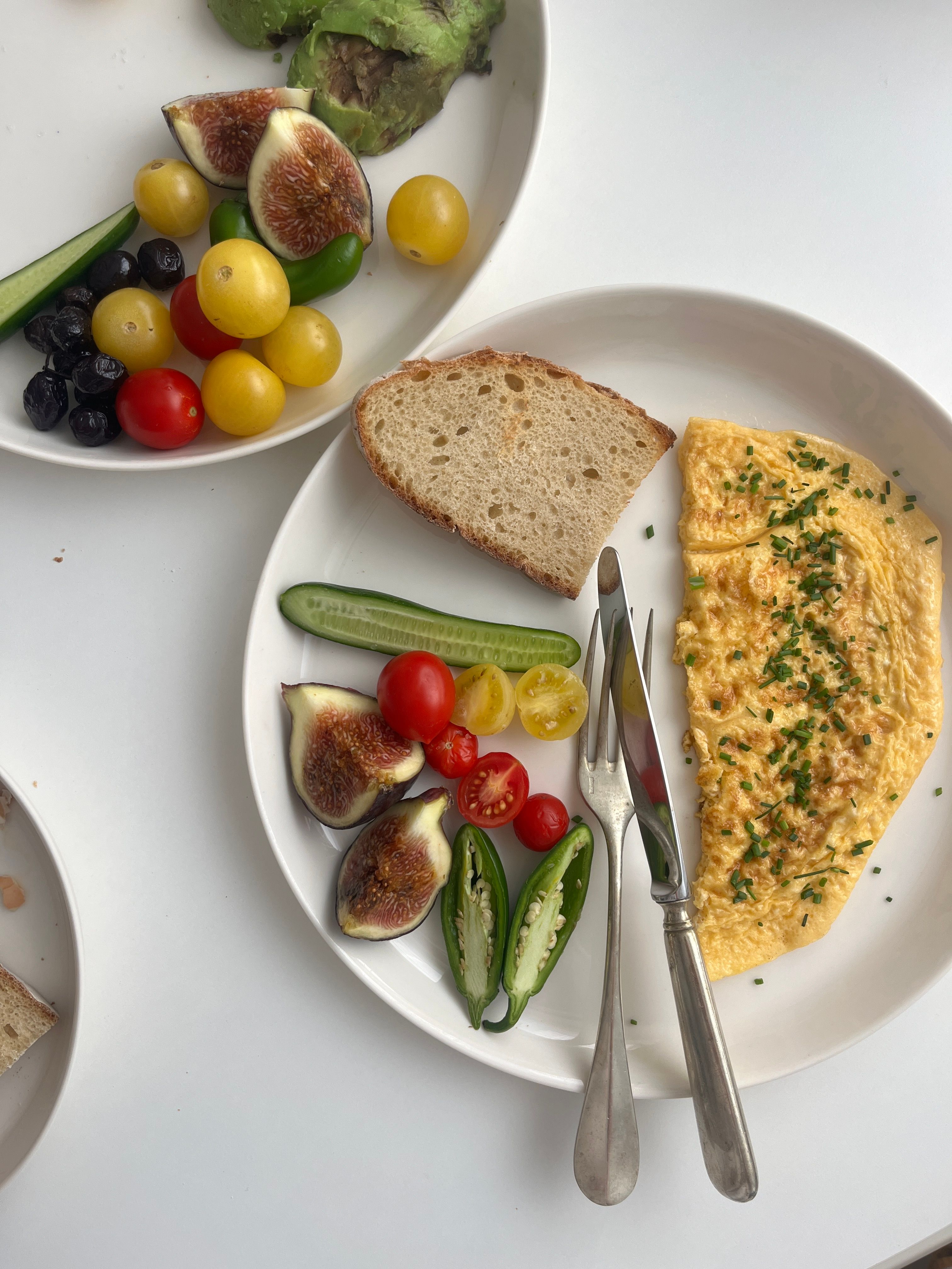 A vibrant breakfast featuring omelette, fresh vegetables, figs, and bread on a white plate.