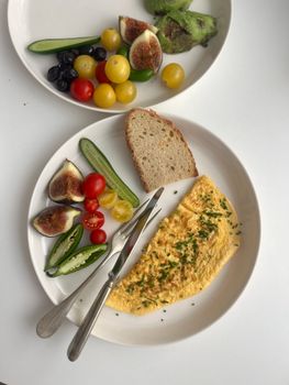 Colorful breakfast plate with omelette, fresh figs, and vegetables on a white table.