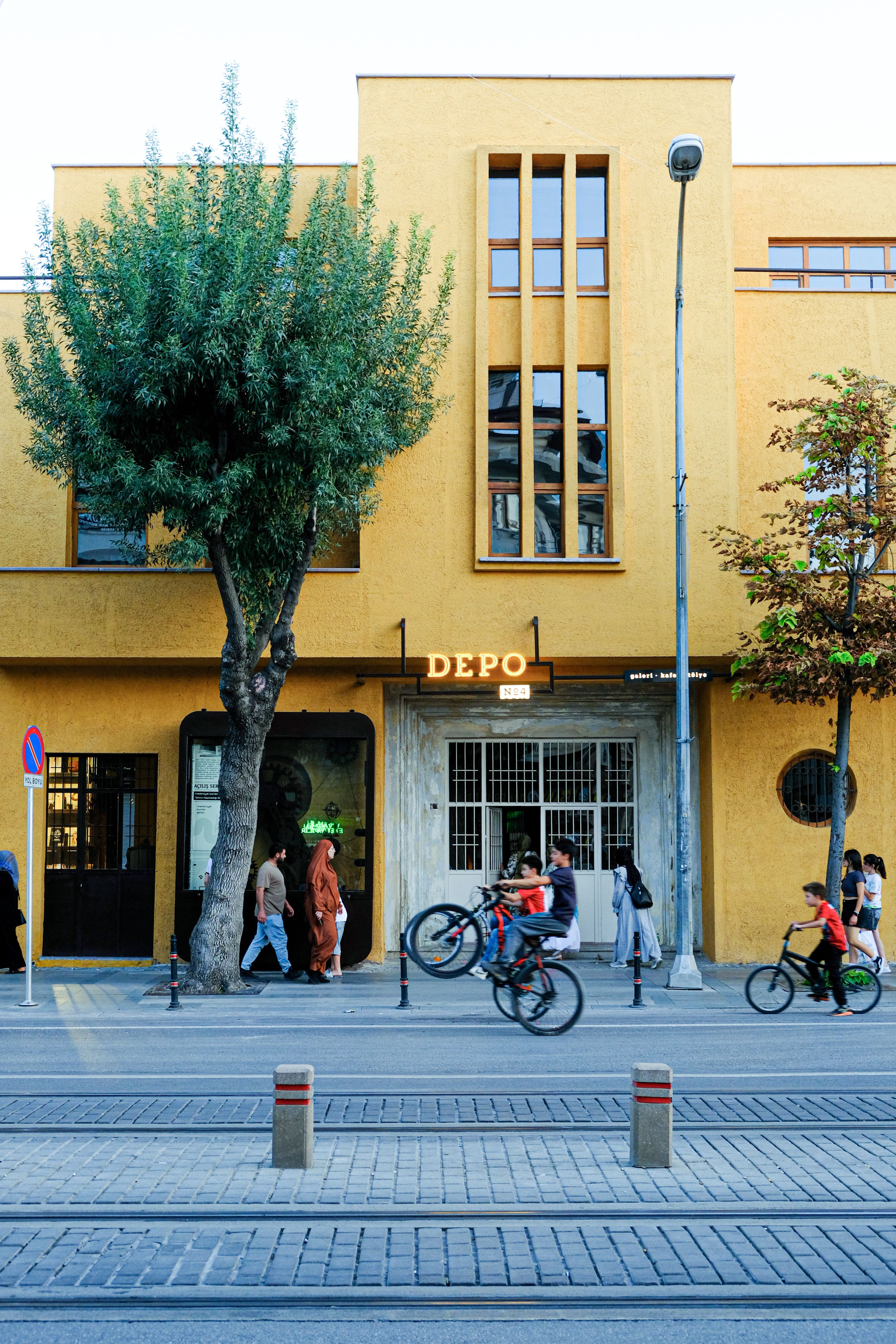 Vibrant city street with people walking and cycling past a colorful modern building.
