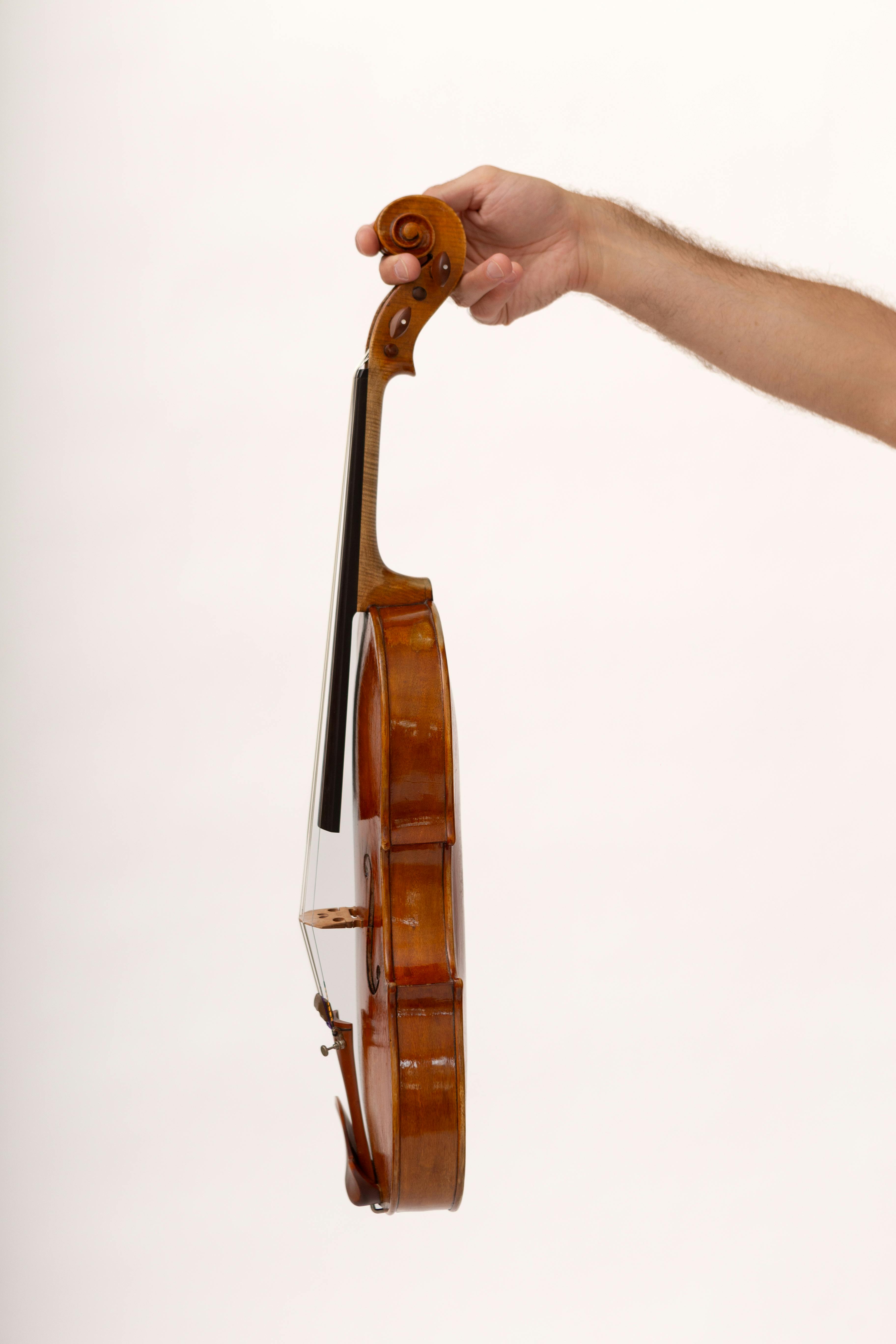 Side view of a violin held in a hand against a plain background.