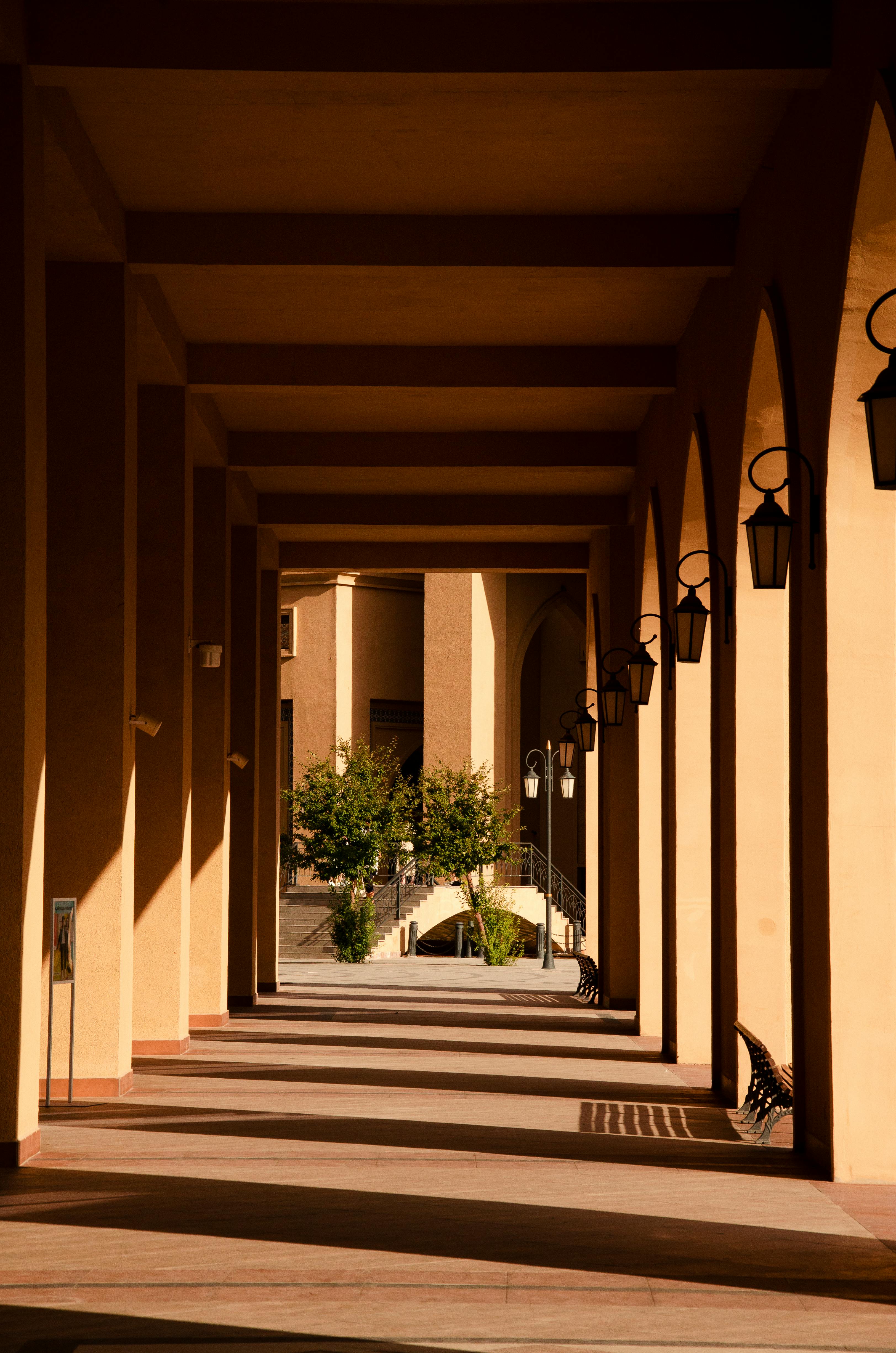 Sunlit hallway with arches casting shadows, evoking historic architectural beauty.