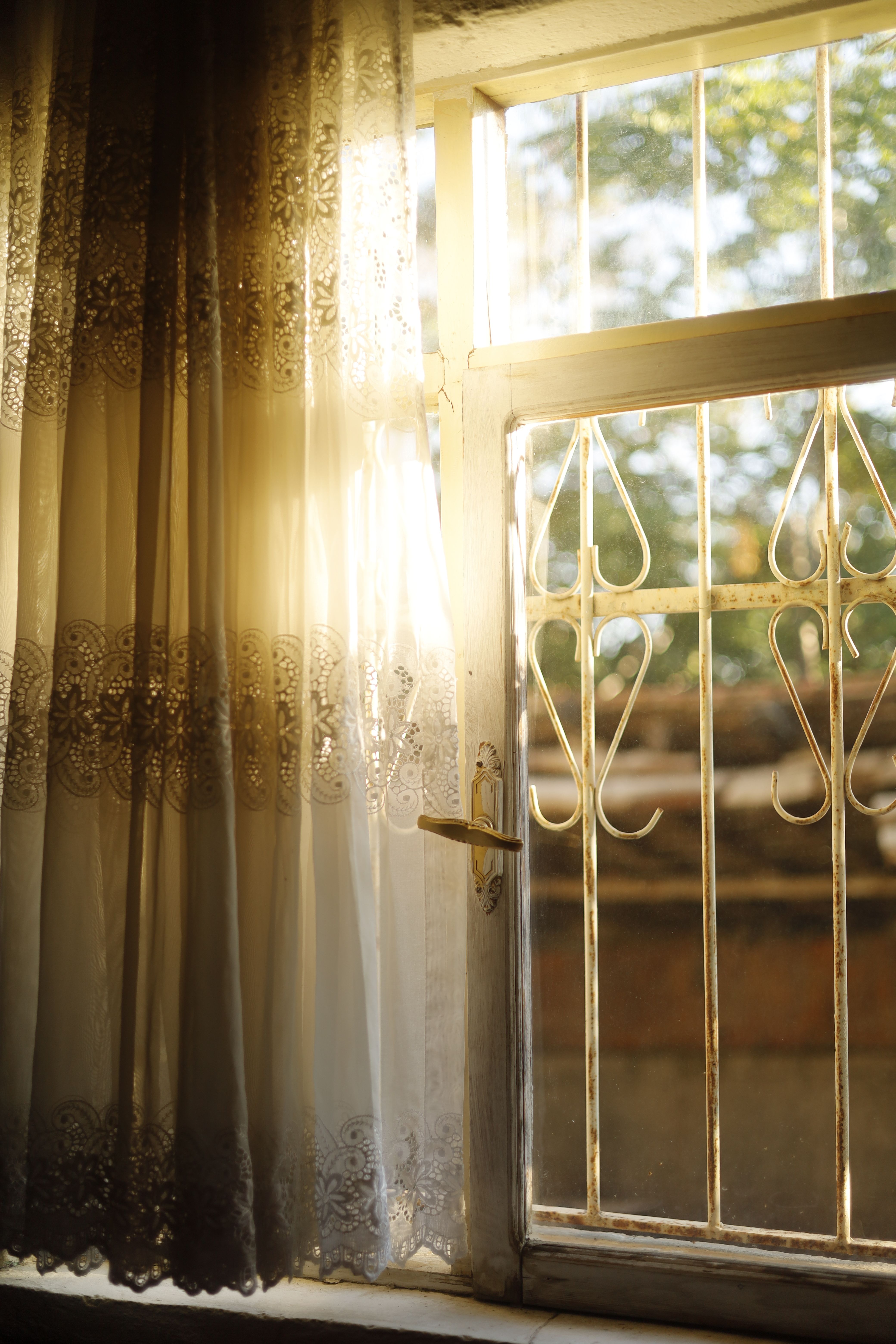 Beautiful sunlit vintage window with ornate lace curtains casting a warm glow indoors.