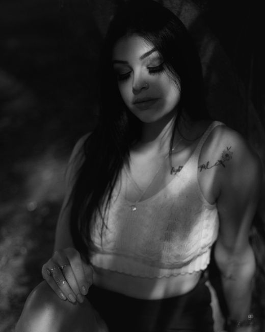 Monochrome portrait of a tattooed woman sitting elegantly in dappled light.