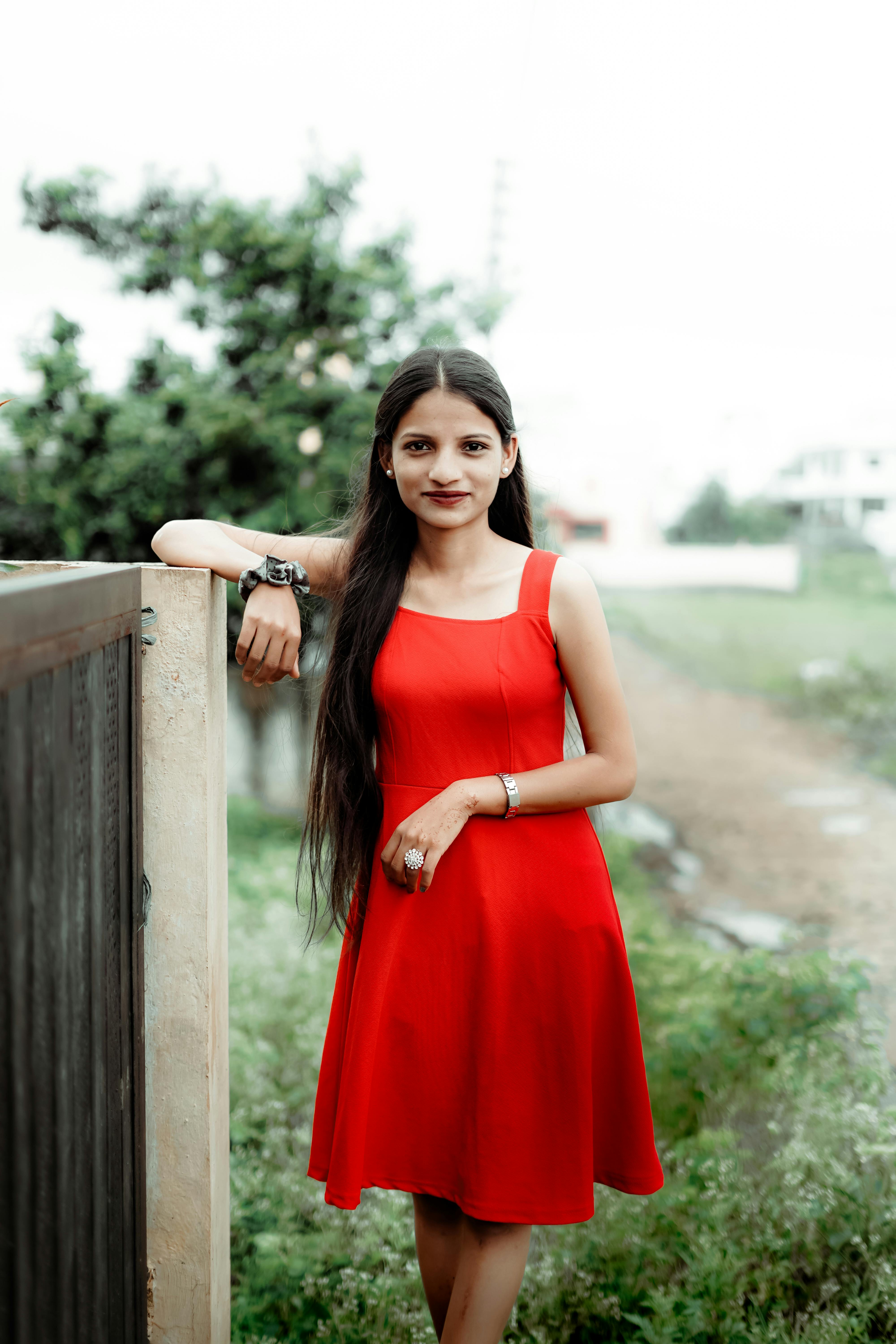 Confident young woman in a red dress enjoying a summer day outdoors.