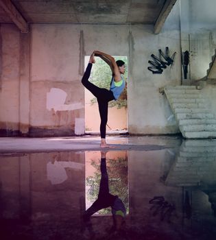 A woman performs yoga in an abandoned building with a reflective puddle, symbolizing balance and tranquility.