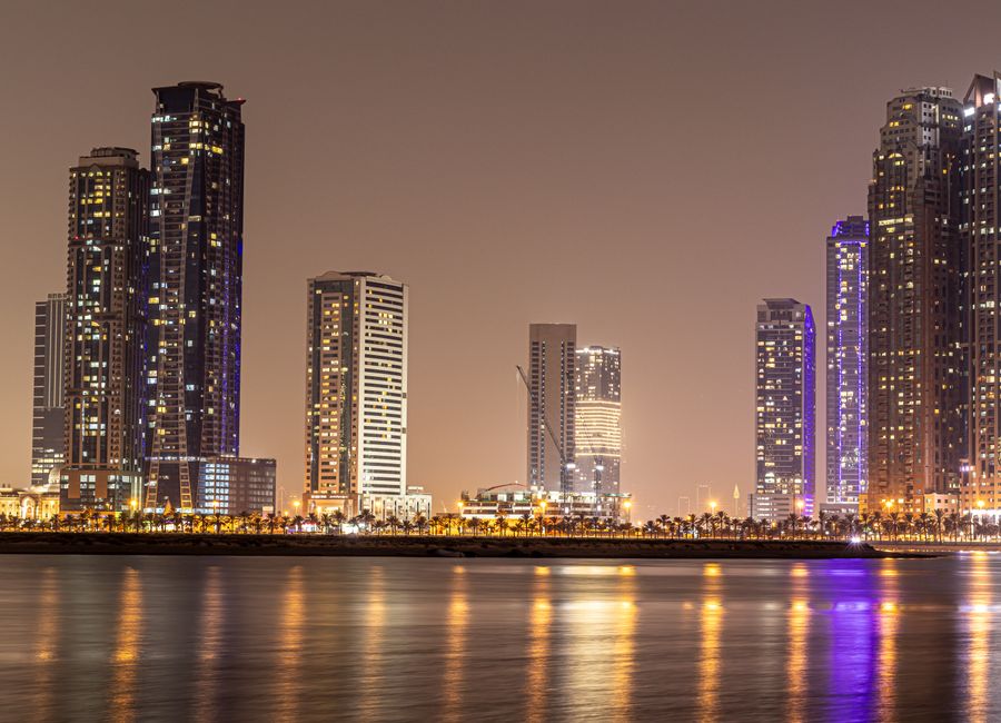 Stunning night view of Sharjah's modern skyline reflected in calm water.