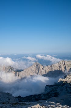 A breathtaking view of Slovenian mountains rising above clouds under a clear blue sky.